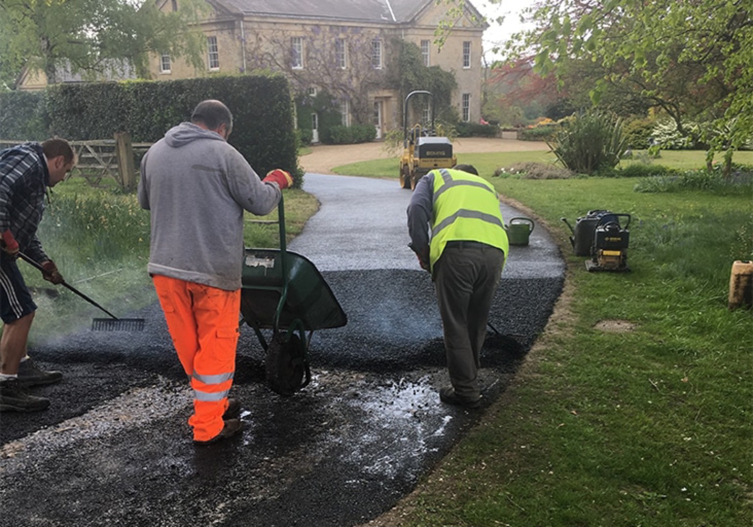 Team using a wheelbarrow and rakes to hand lay hot tarmac on a large driveway in Ayrshire