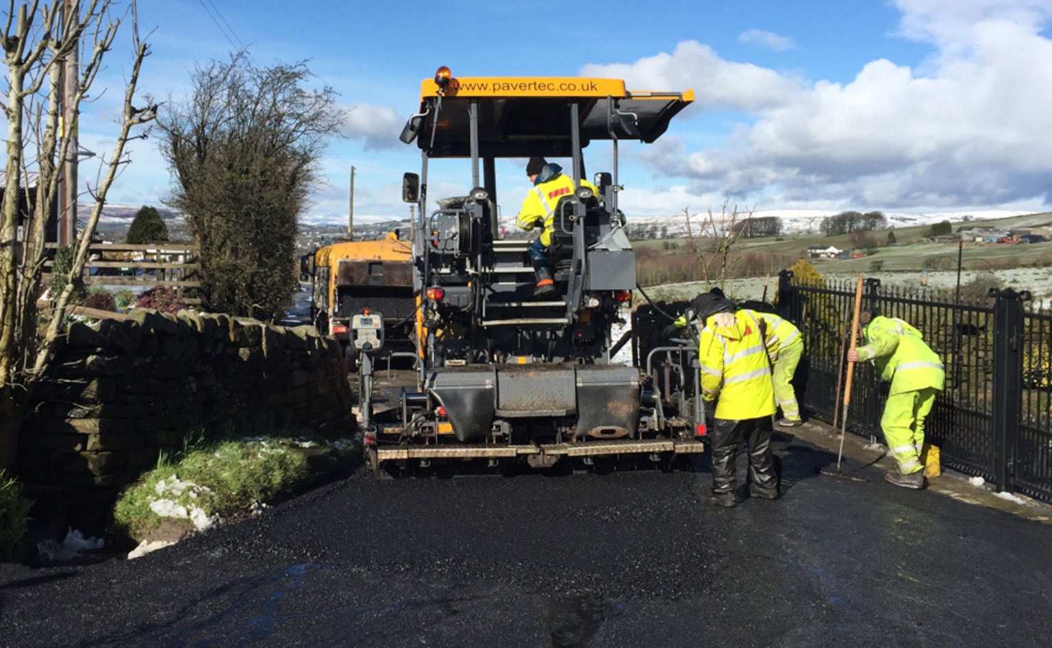 Paver and surfacing team laying hot rolled asphalt through a farm entrance near Elgin in Morayshire, Scotland