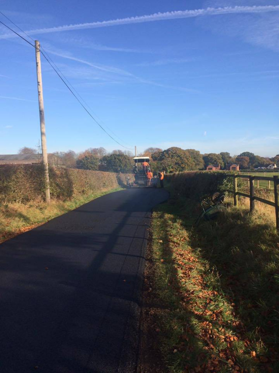 New tarmac along a rural lane with fields and hedges on either side