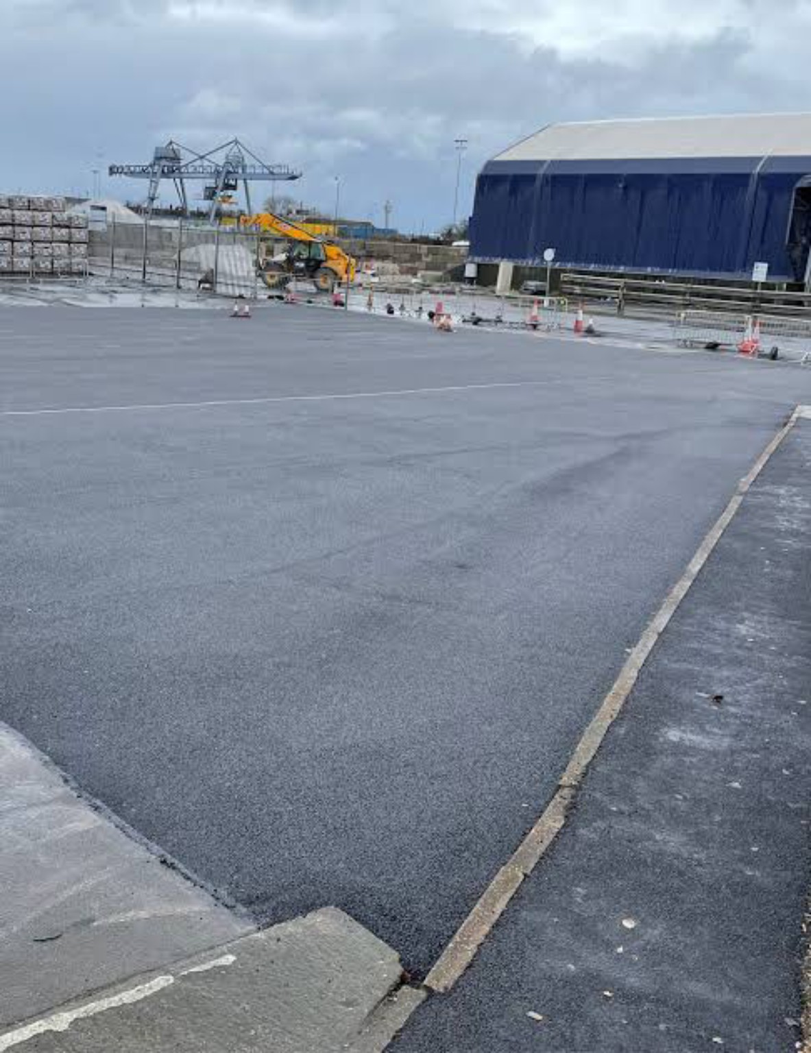 Completed hot tarmac repair across a shipping yard in Fraserburgh, with industrial buildings and cranes beyond