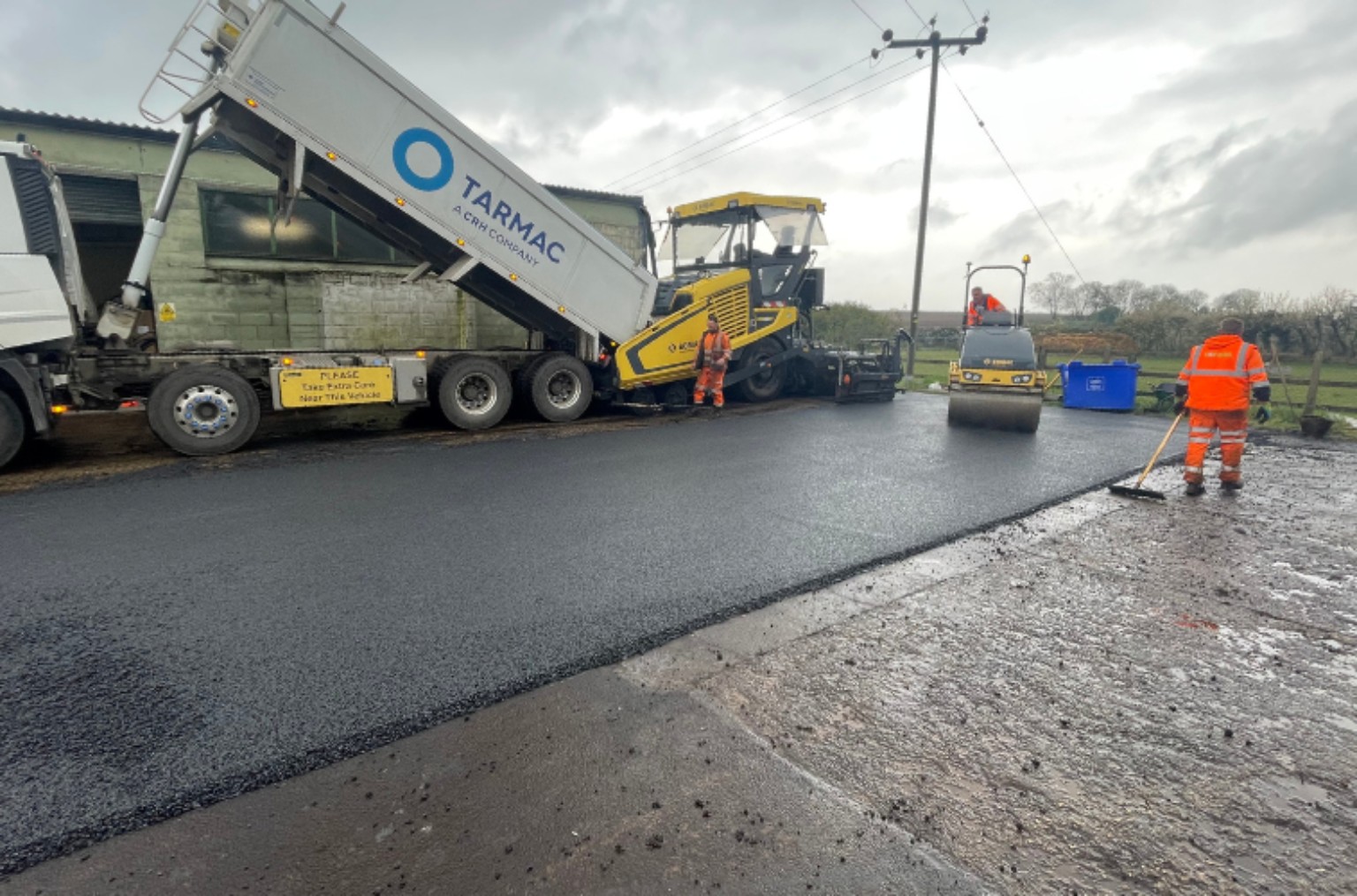 Tipper supplying a tarmac paver at a commercial factory in Glasgow, with a roller on the new surface