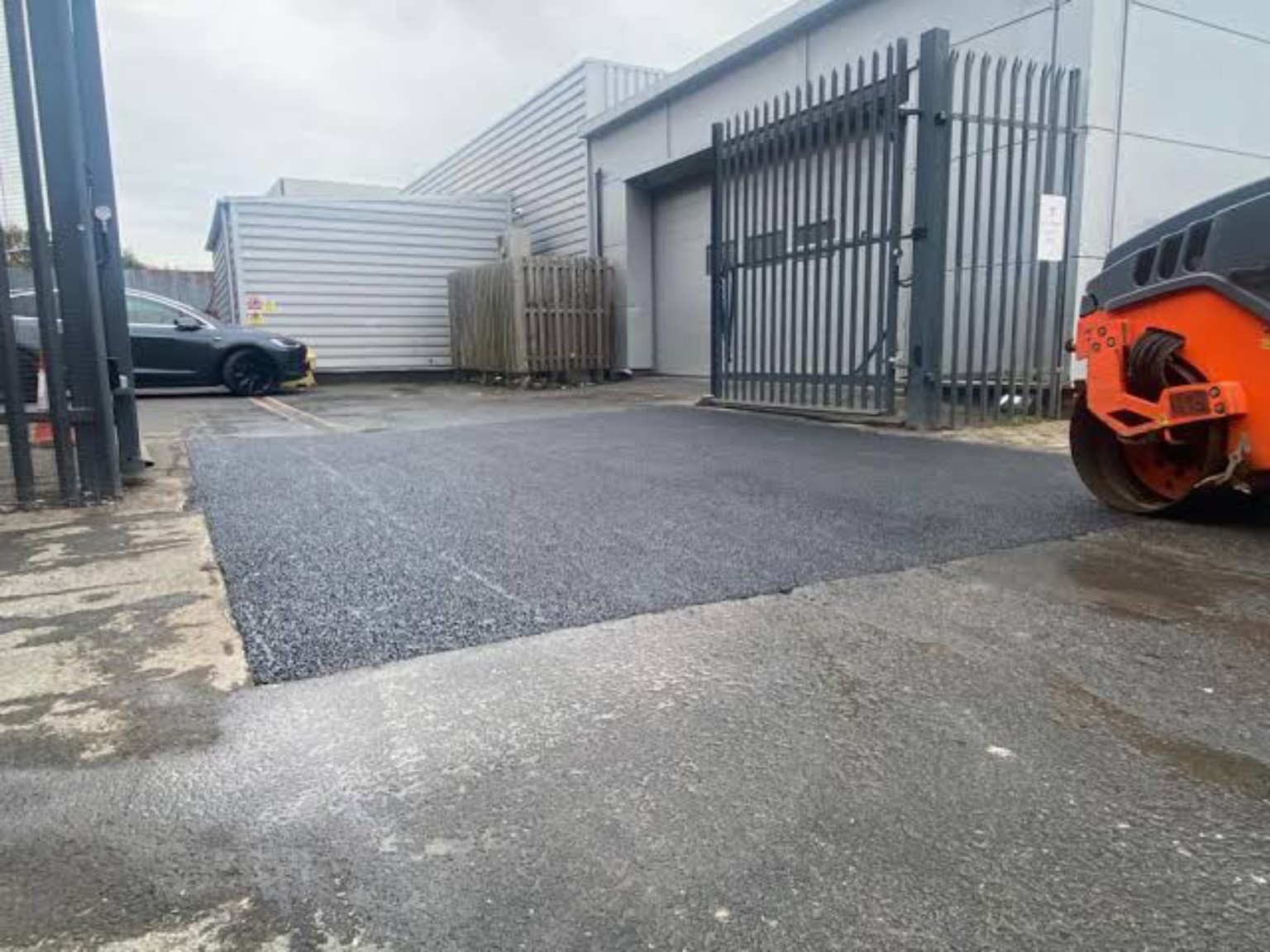 New asphalt repair across a gated factory and warehouse entrance in Grangemouth, with a roller beside the surface