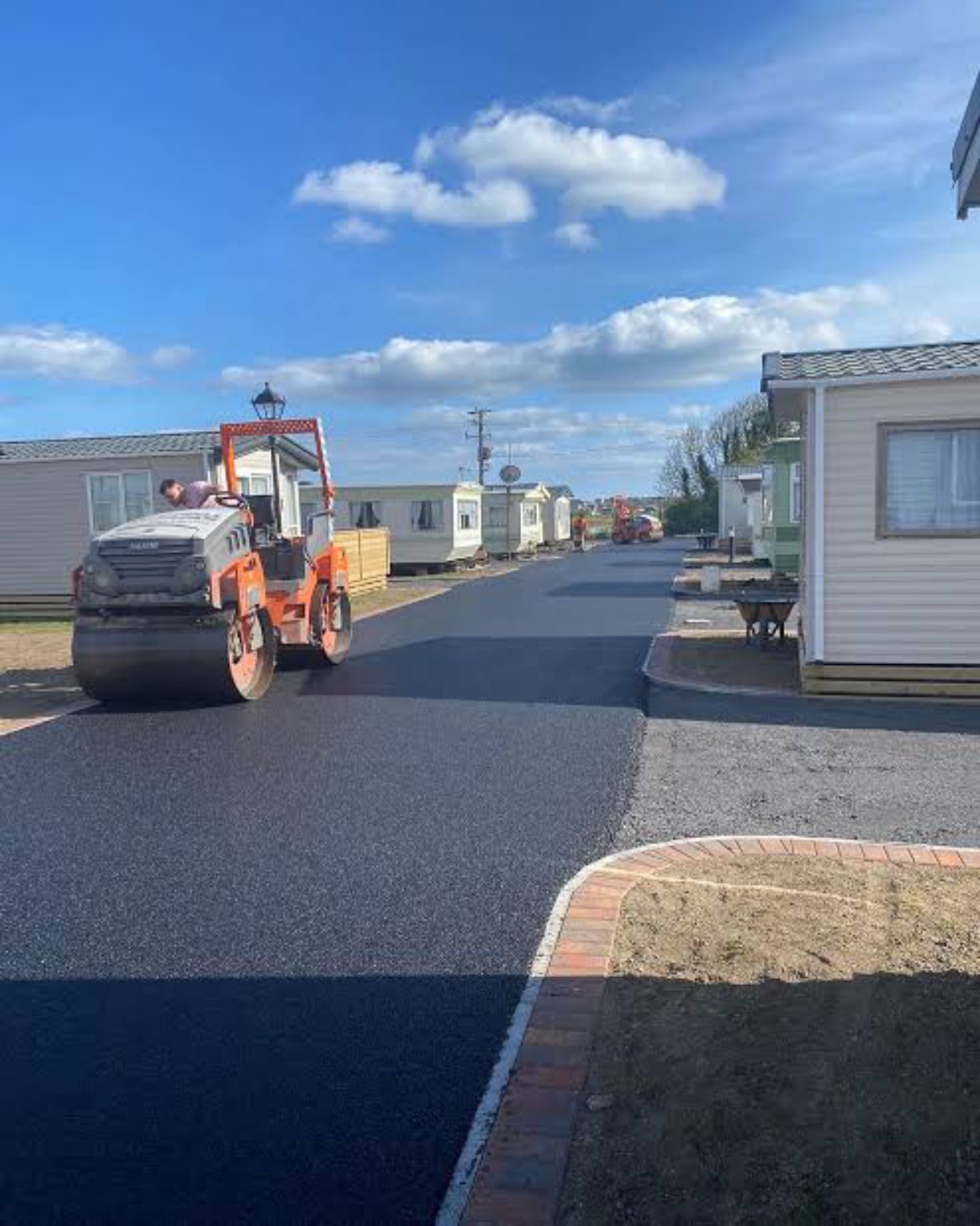 Roller compacting a freshly machine-laid tarmac road between caravans at a Loch Lomond caravan park