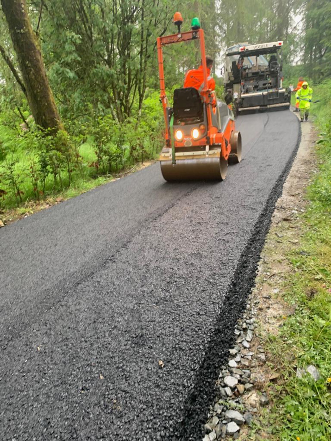 Roller following a paver on a wooded manor house and estate access road in Lochgilphead, Scotland