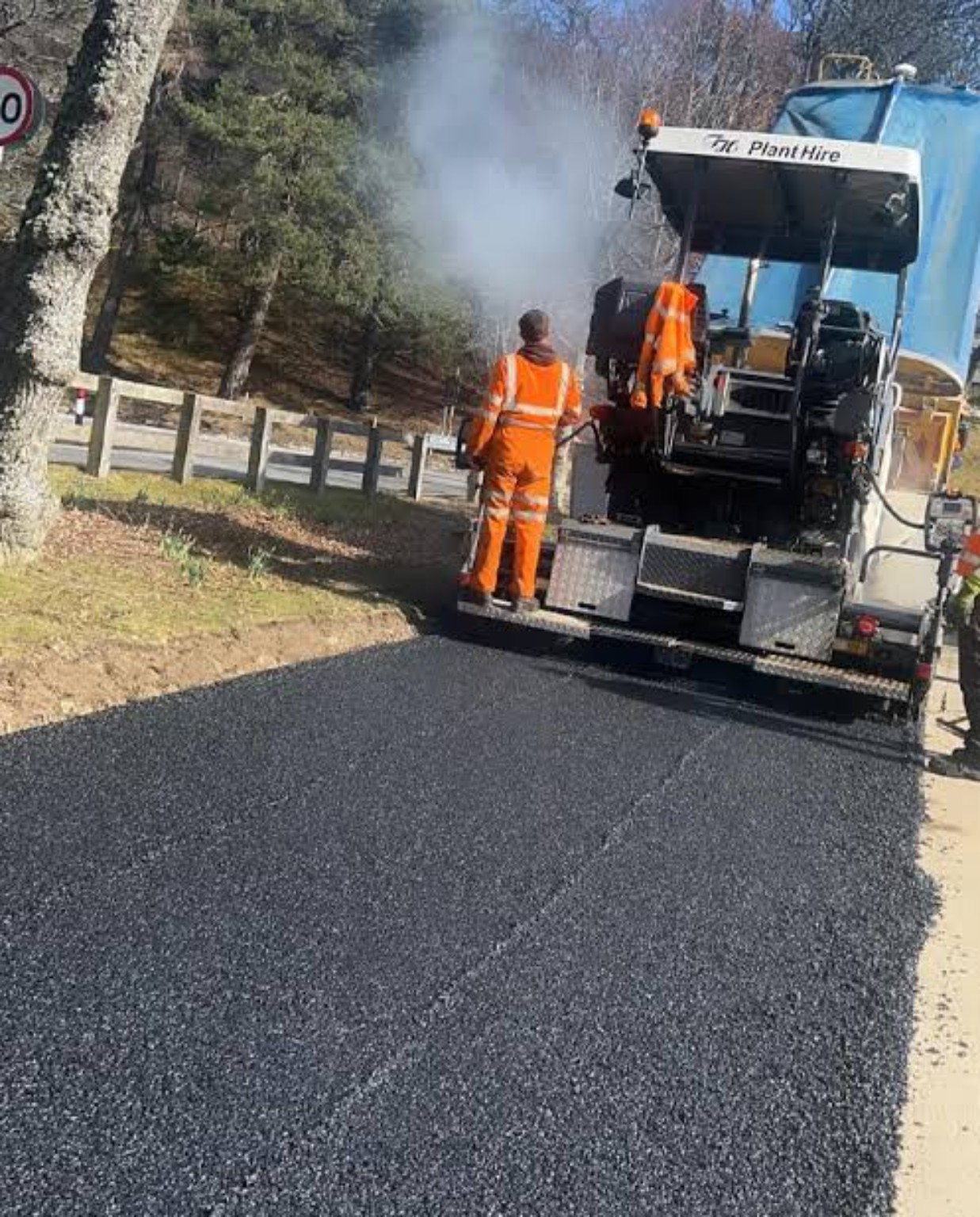 Asphalt paver and worker laying hot tarmac on a rural lane