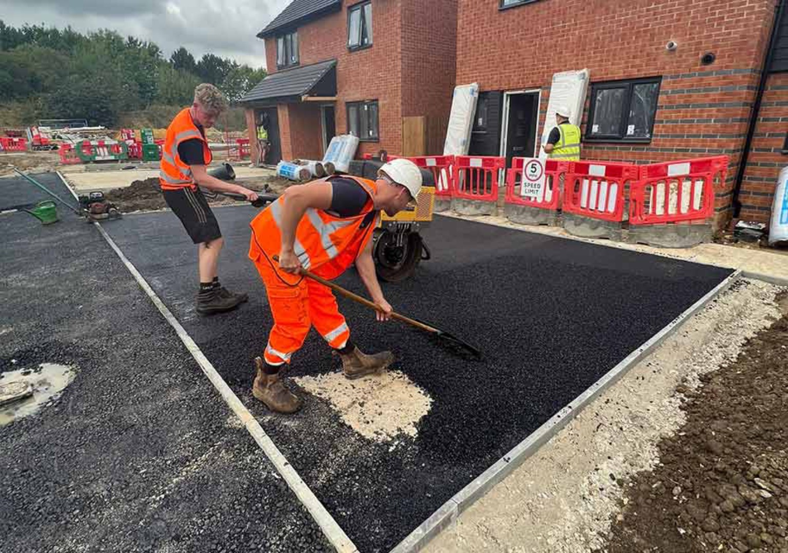 Surfacing team spreading and compacting tarmac on a driveway beside new brick homes in Paisley