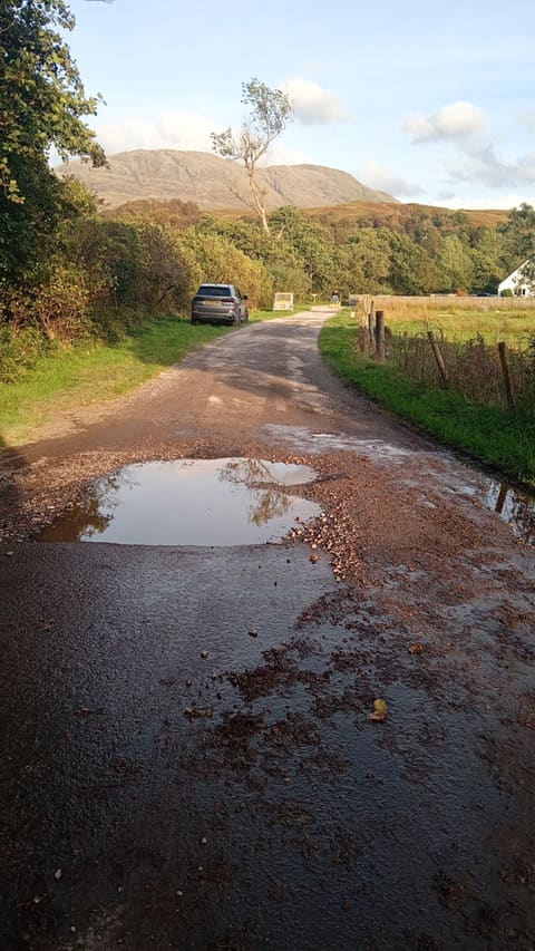 Private shared roadway near Fort William before work, showing water-filled potholes