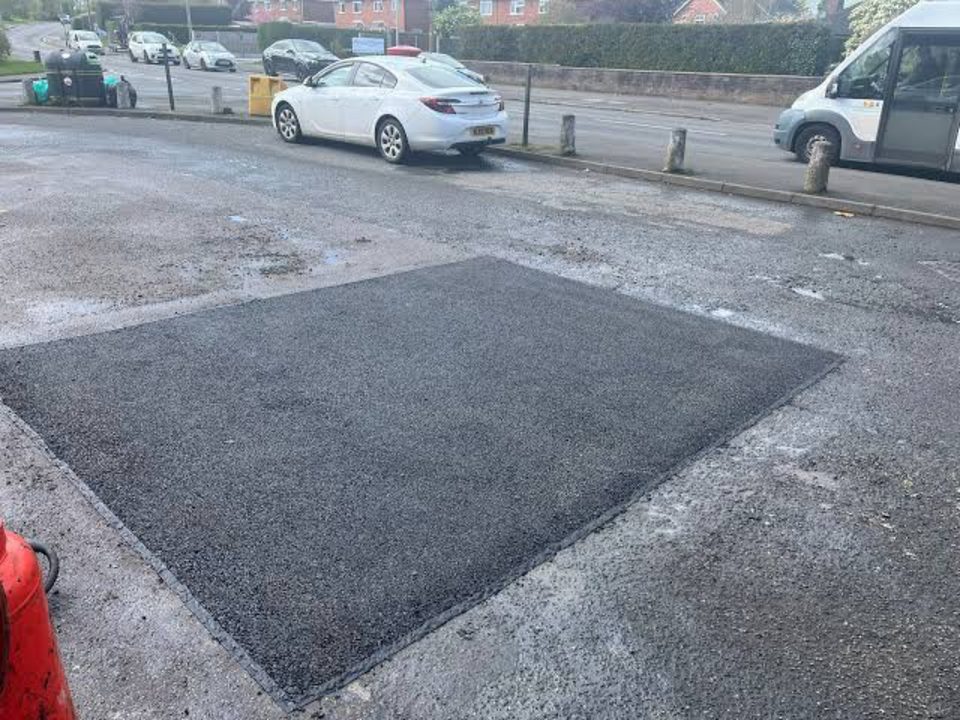 Rectangular tarmac patch repair in a public carriageway in Stirling, with parked vehicles beyond