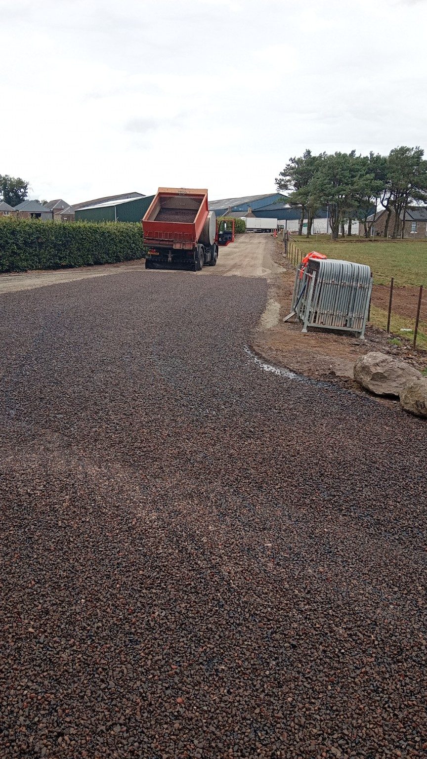 Freshly laid dark tar-and-chip surface at the same Balmachie Farms entrance, with the combi unit continuing along the access road