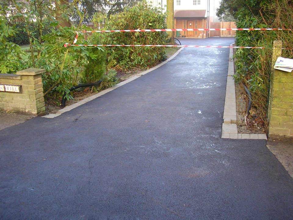 Resurfaced tarmac driveway with pale block edging along a curved landscaped entrance