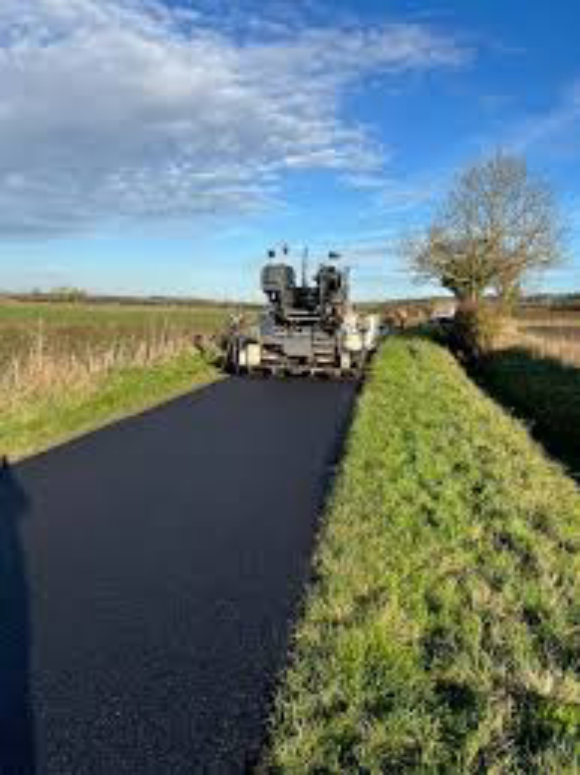 Paver laying hot tarmac along a private farm access road between fields and grass verges in Inverness, Scotland