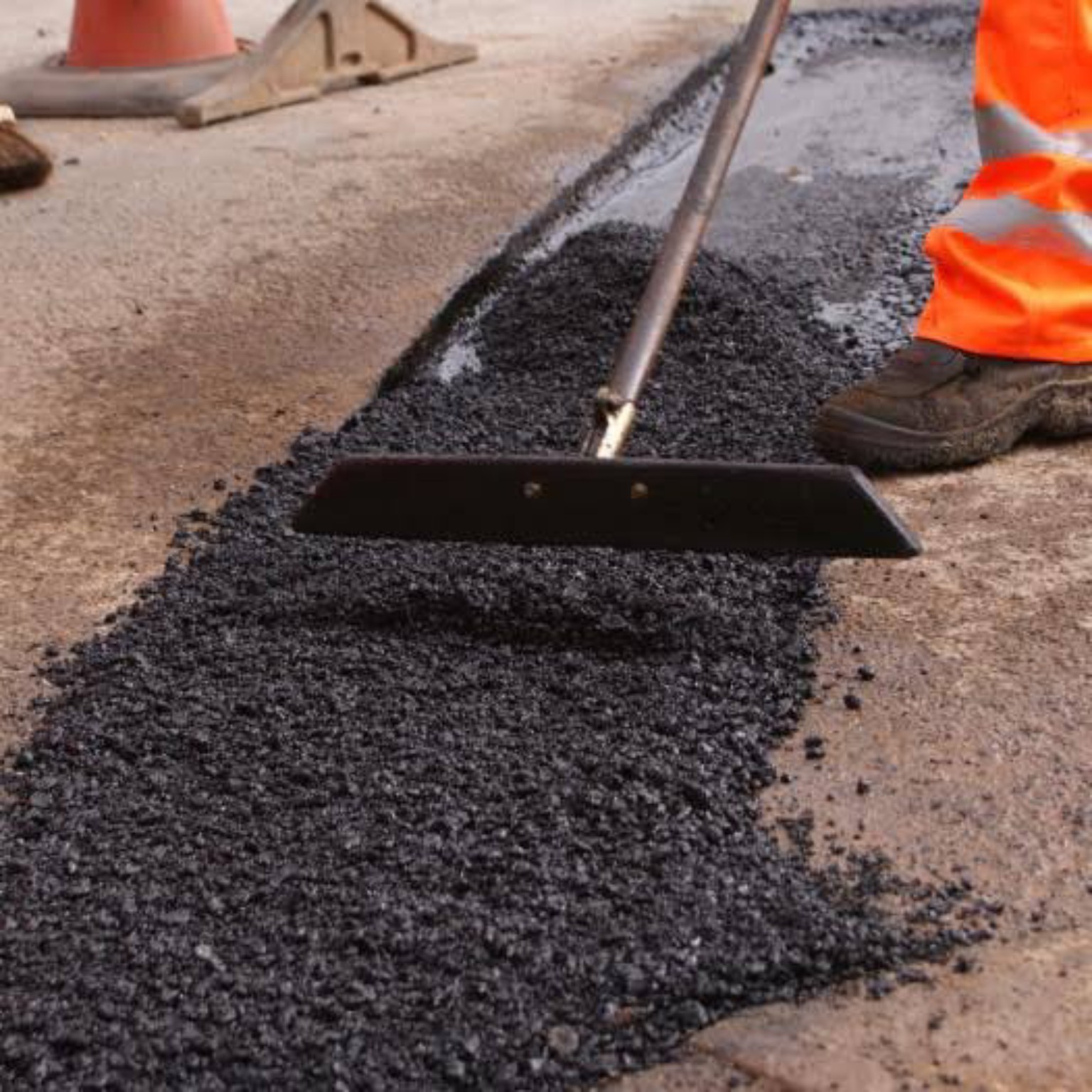 Worker raking tarmac along a narrow cable trench during reinstatement work in Scotland