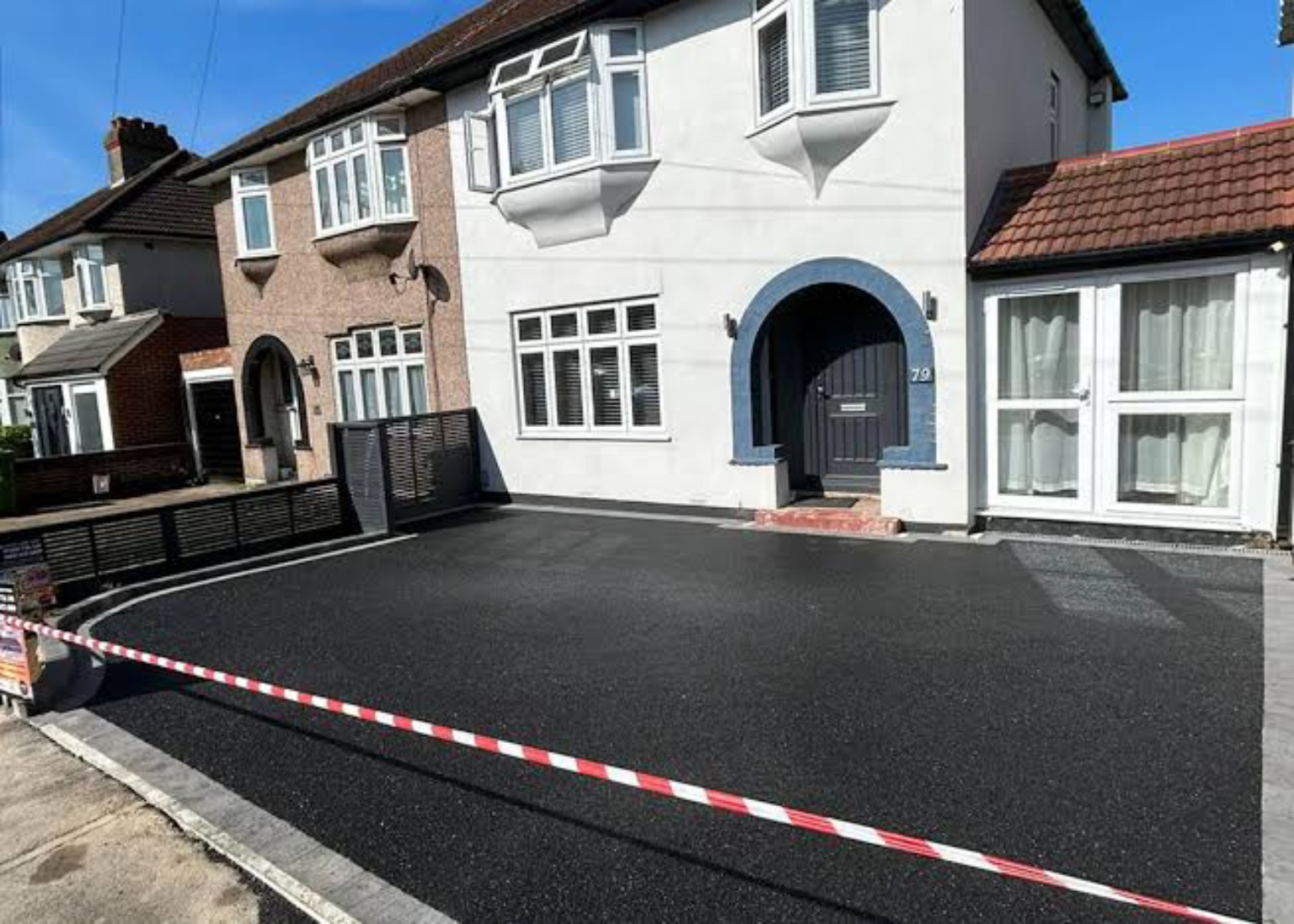 Completed broad tarmac driveway in front of a white house with grey block edging