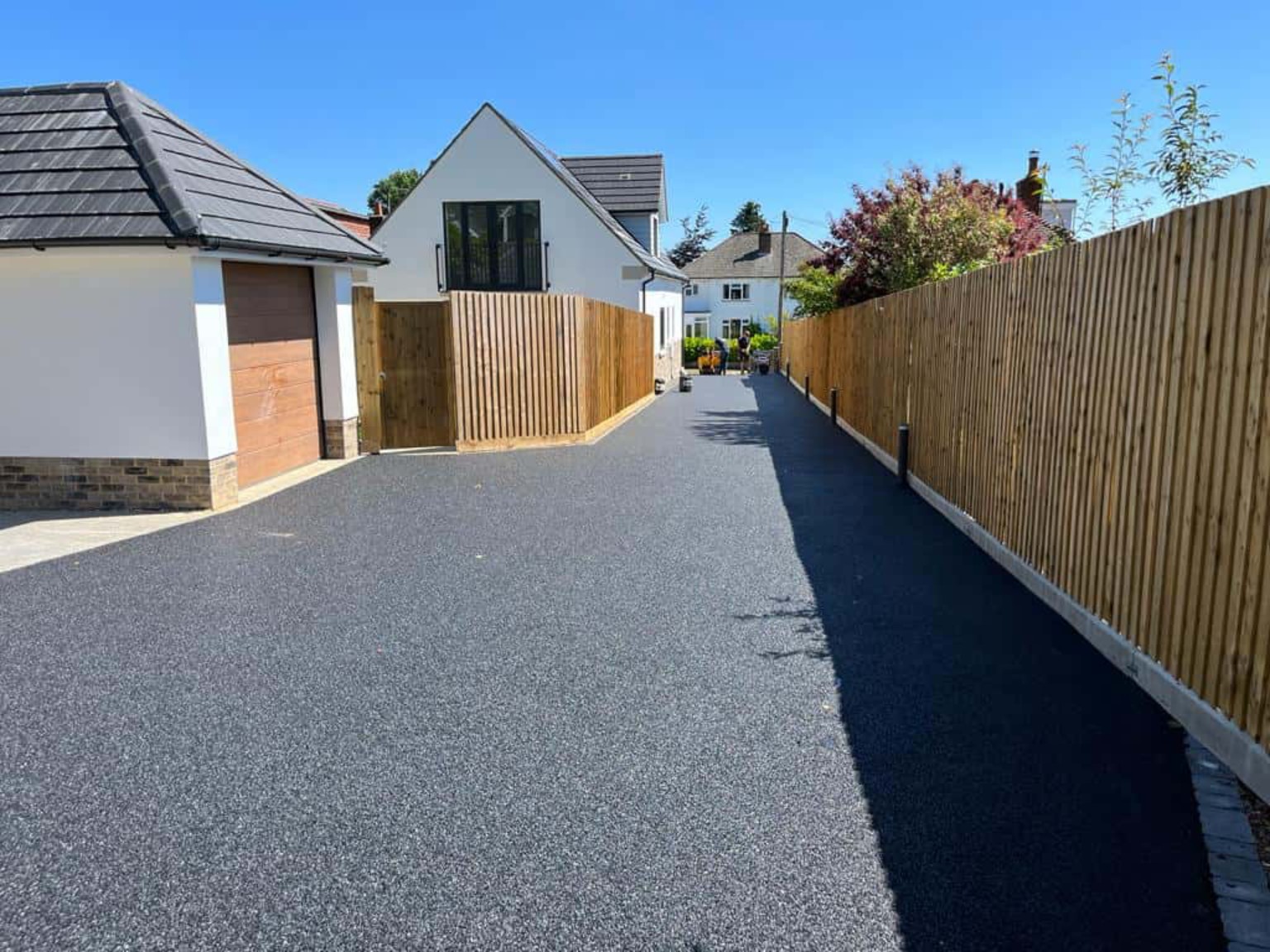 Tarmac garage forecourt connected to a long access driveway between timber fences