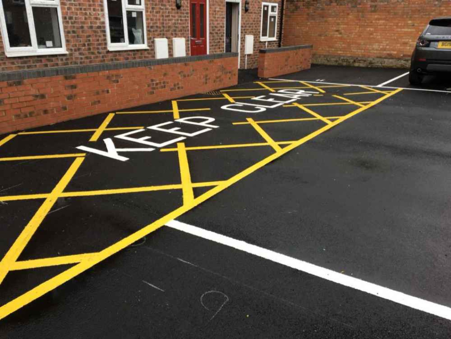 Tarmac parking bays and a marked keep-clear area beside a building entrance