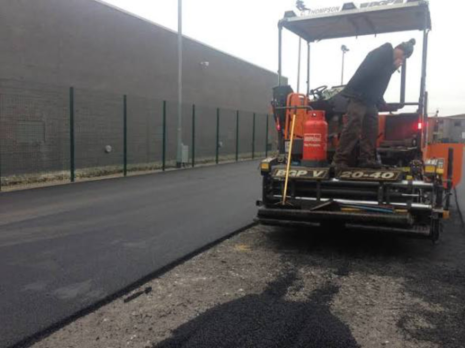 Paver laying tarmac on a road beside the perimeter fence outside a new prison in Yorkshire